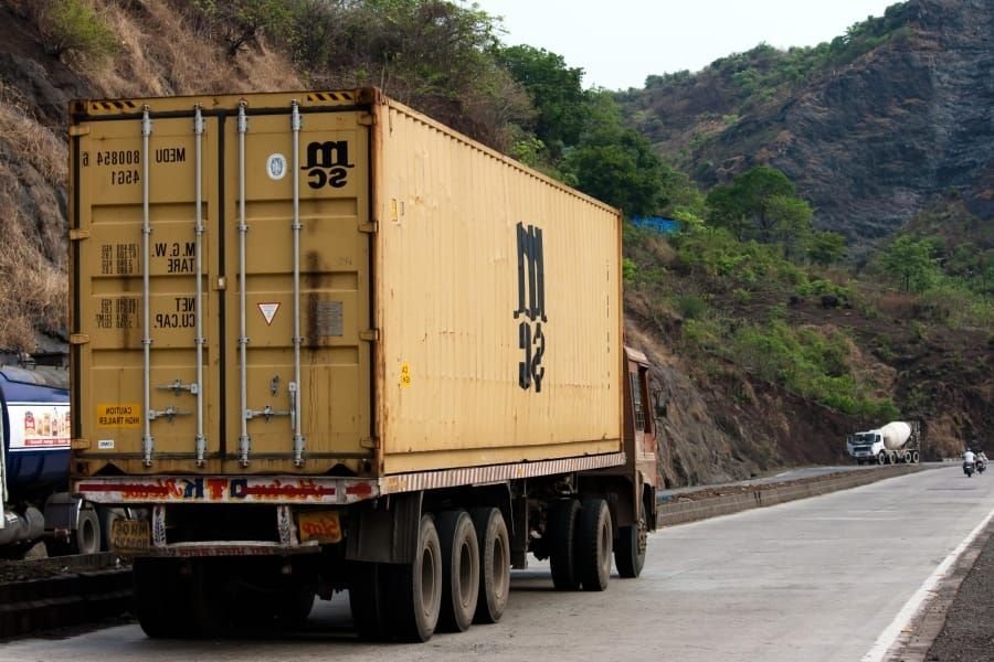Yellow container trailer on a hill road, typical of long-distance carriers heading from Delhi towards Pune